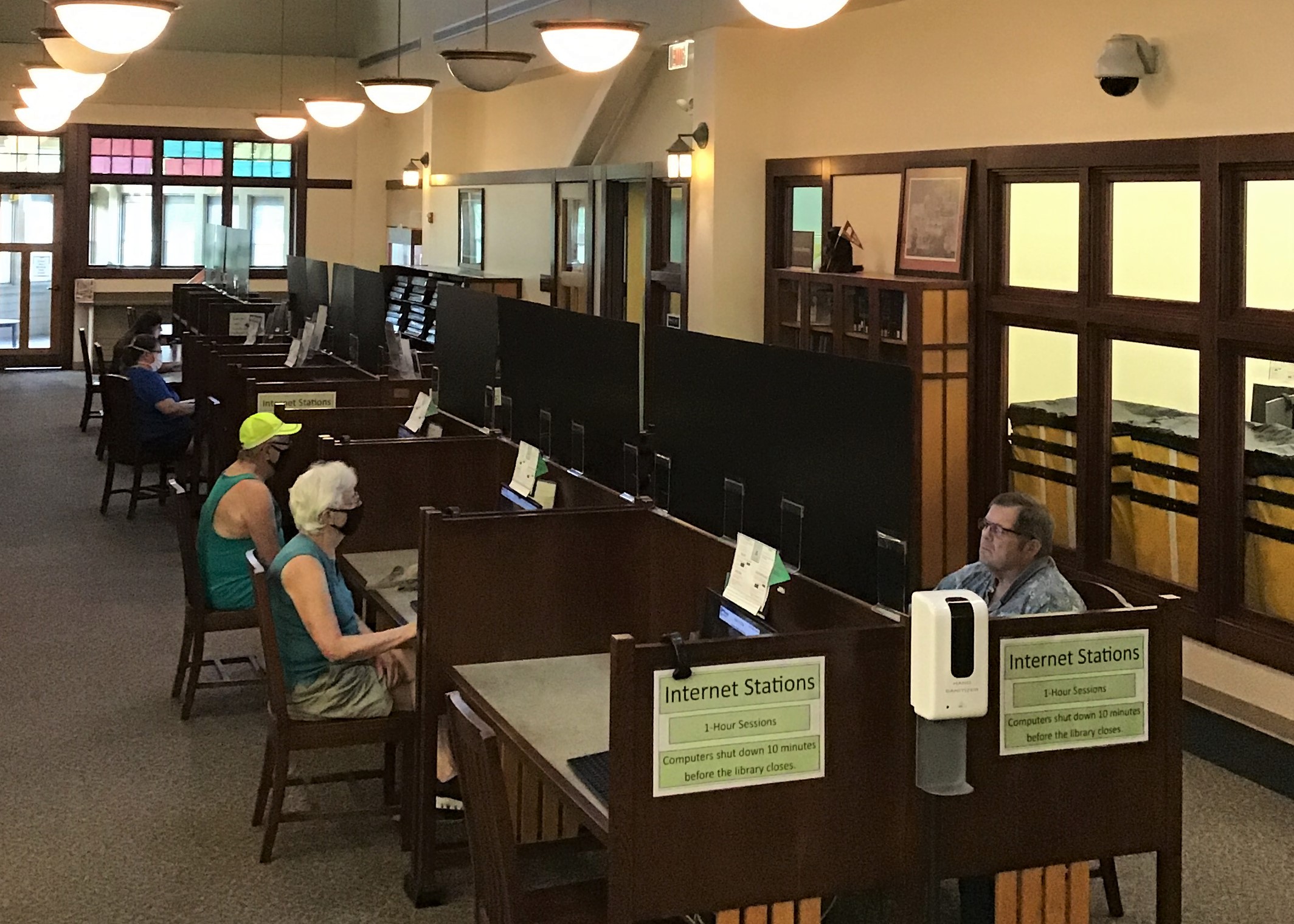 people sit at computers in the library while sunlight streams in from windows behind