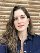 photo of the artist, a white woman with brown hair standing in front of a brick wall