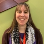 Erin Williams Heart, Head of Adult Services. White woman with brown hair. Black and white scarf, red staff badge, purple shirt and cardigan. 